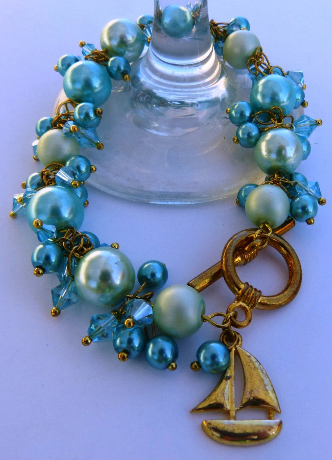 Bracelet with blue and green beads and gold accents on a shell background